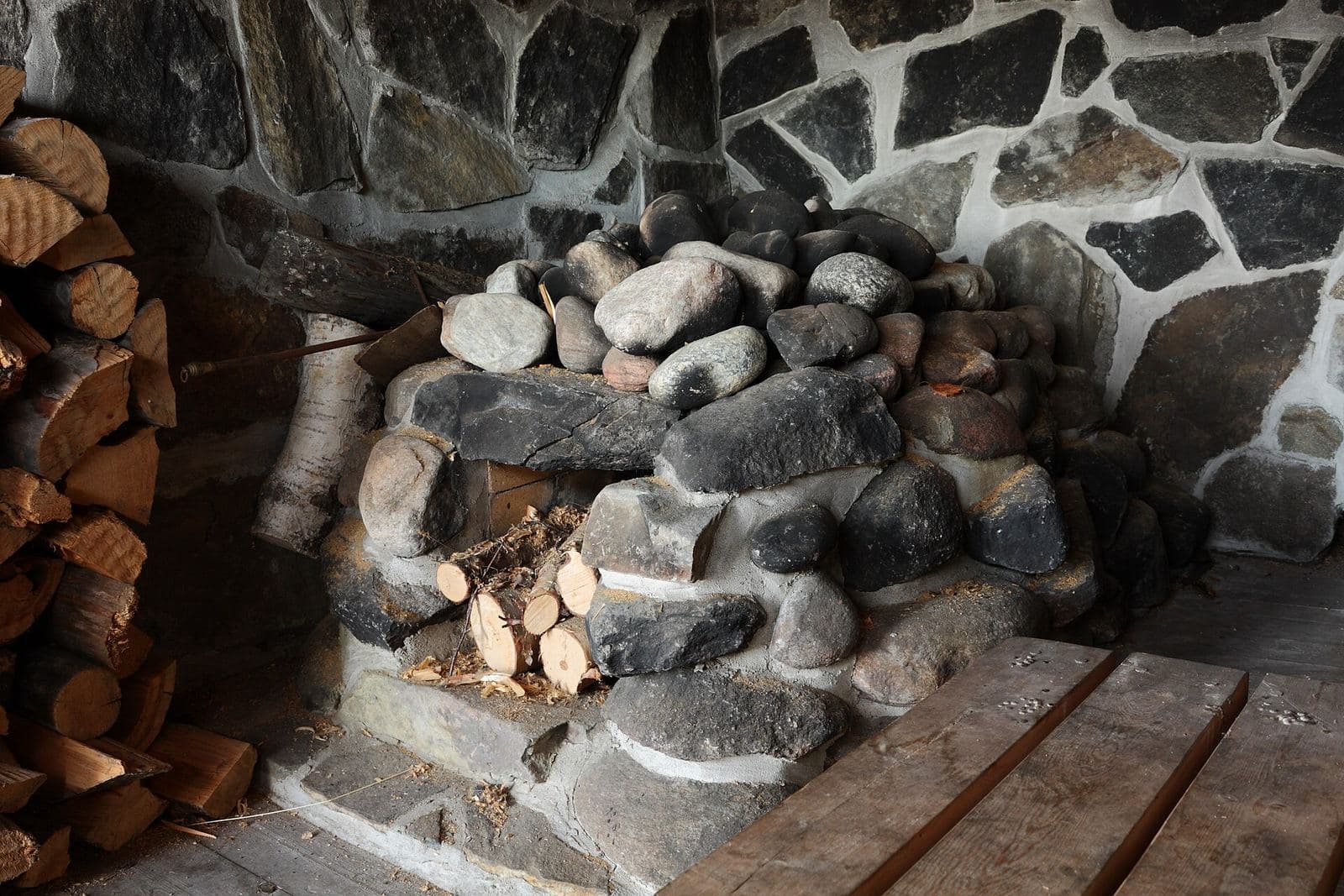 A stone sauna stove with firewood stacked beside it